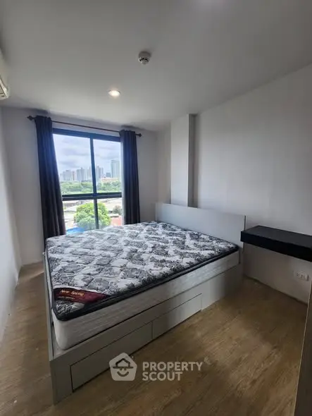 Modern bedroom with large window offering city view, featuring a comfortable bed and sleek wooden flooring.