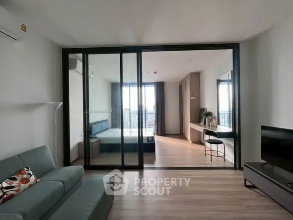 Modern open-plan living room with glass partition to bedroom, featuring sleek furniture and natural light.