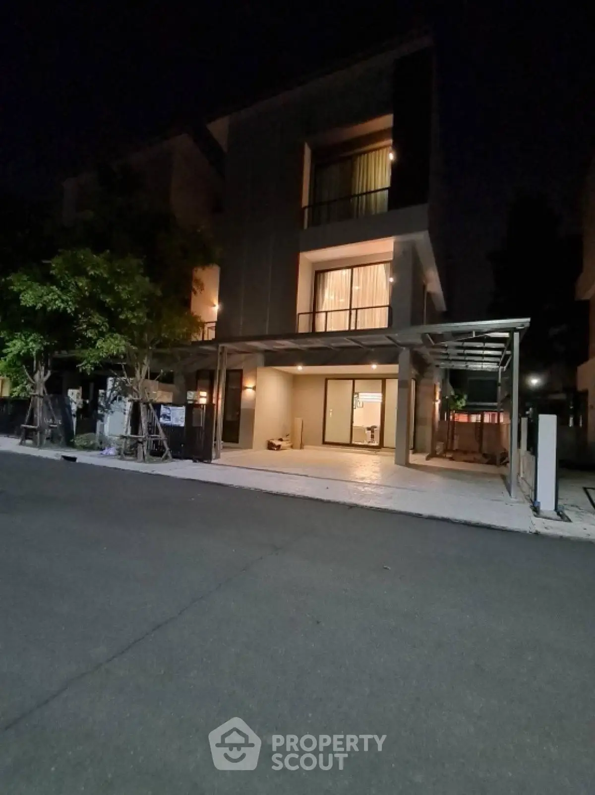 Modern three-story house with illuminated windows and carport at night