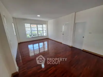 Spacious empty room with polished wooden floors and large window view.