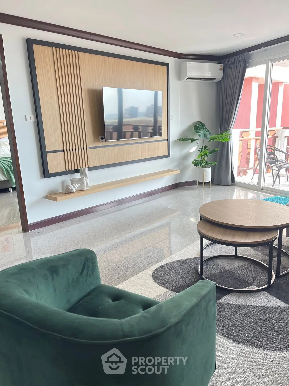 Modern living room with stylish decor and balcony view, featuring a green armchair and sleek TV setup.