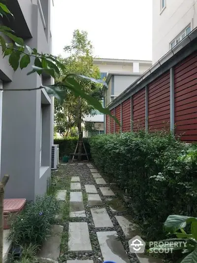 Charming garden pathway between modern buildings with lush greenery and stone path