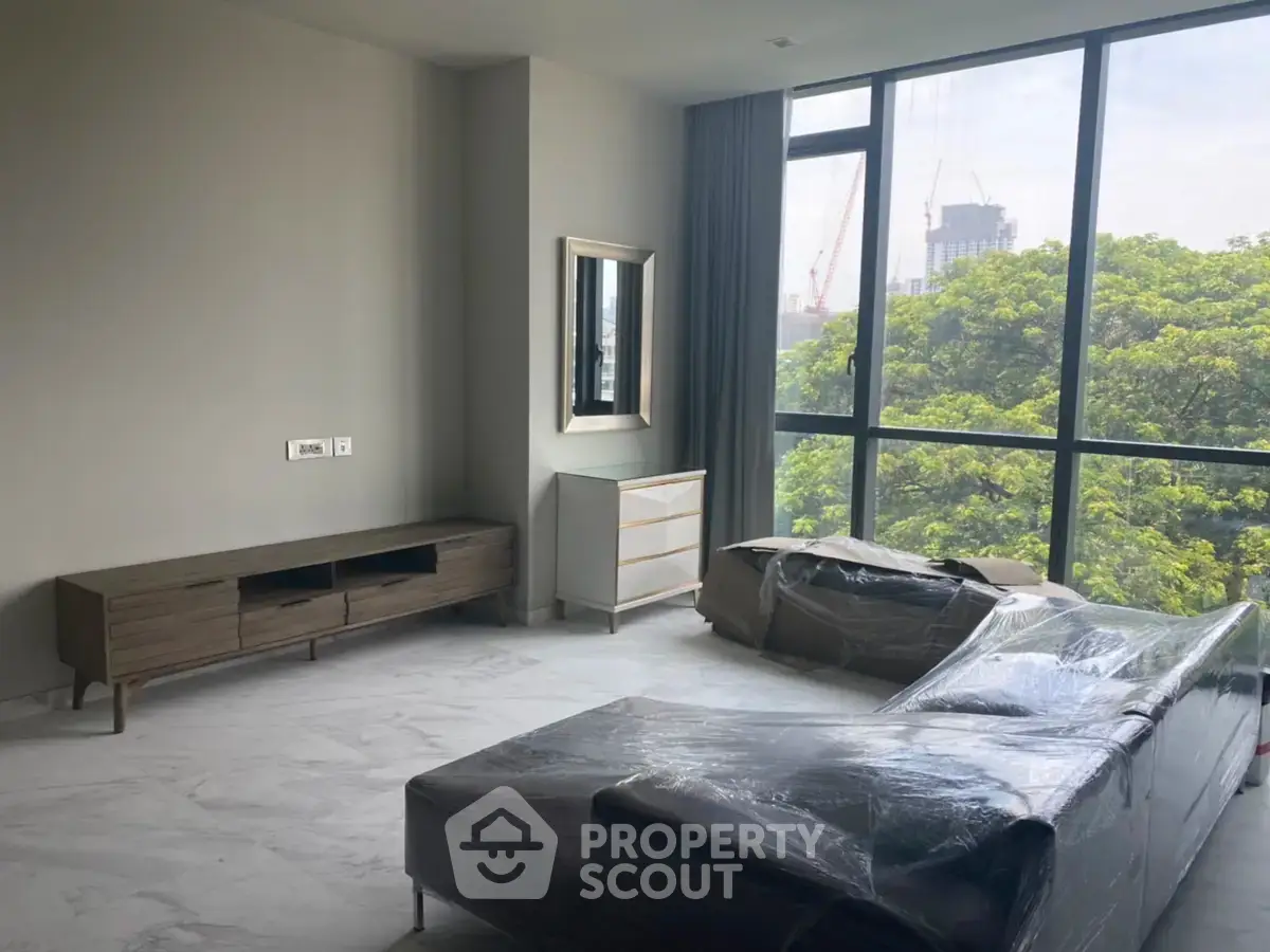 Spacious living room with large windows and modern furniture, offering a serene view of lush greenery.