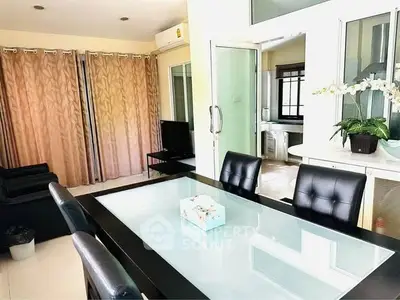 Modern dining area with glass table and leather chairs, adjacent to cozy living room.