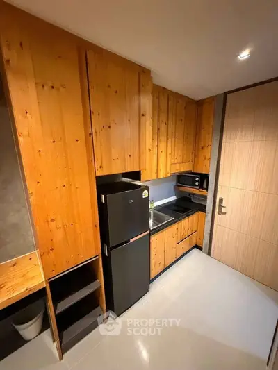 Modern kitchen with wooden cabinets, compact fridge, and microwave in a cozy apartment setting.