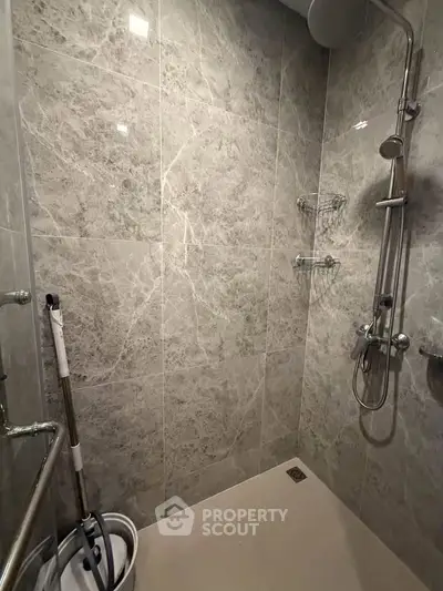 Modern bathroom with sleek marble tiles and rainfall showerhead, showcasing contemporary design and luxury.