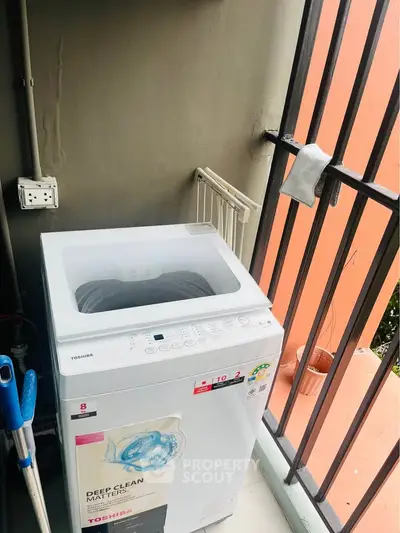 Compact balcony with washing machine and railing, ideal for urban living.