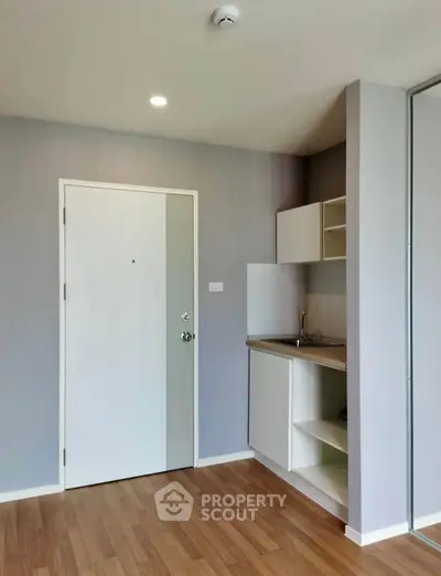 Modern minimalist apartment entrance with sleek kitchen area and wooden flooring.
