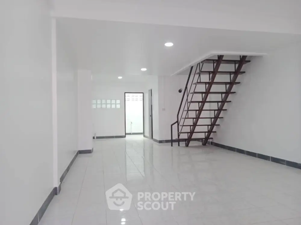 Spacious open-plan interior with sleek staircase and modern white tile flooring.