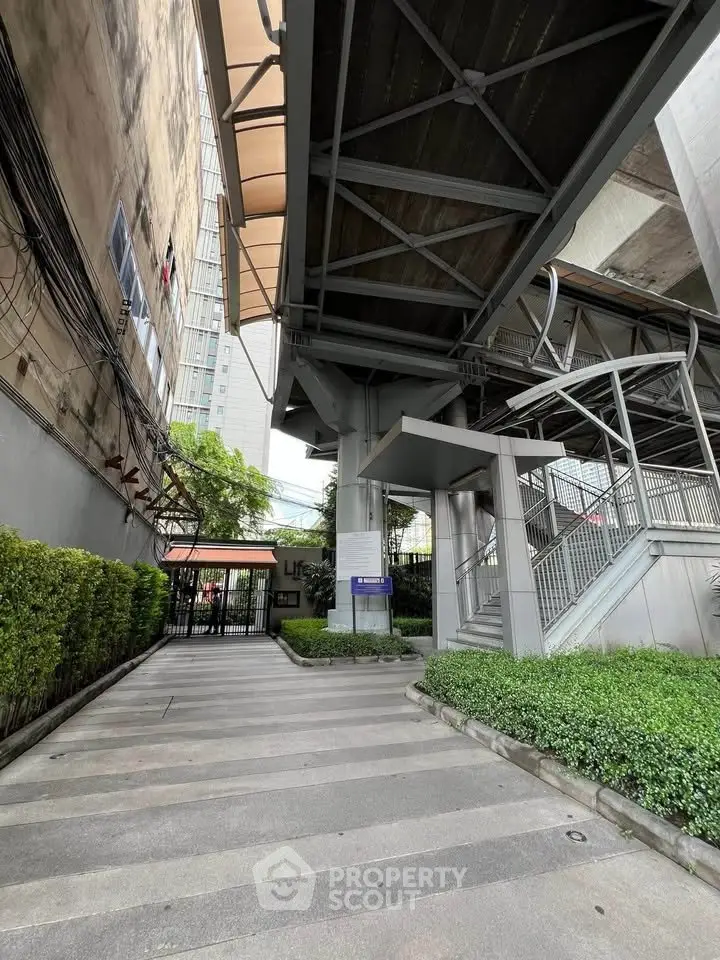 Modern urban entrance with greenery and architectural steel structures.