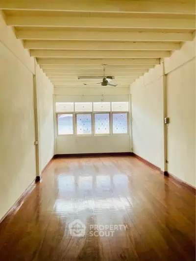 Spacious empty room with wooden floors and large windows, perfect for customization.