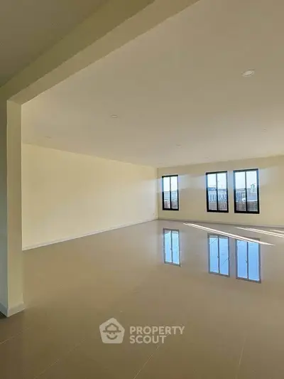 Spacious empty living room with large windows and glossy tiled floor, offering abundant natural light.