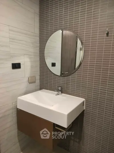 Modern bathroom with stylish sink and round mirror, featuring elegant tile design.