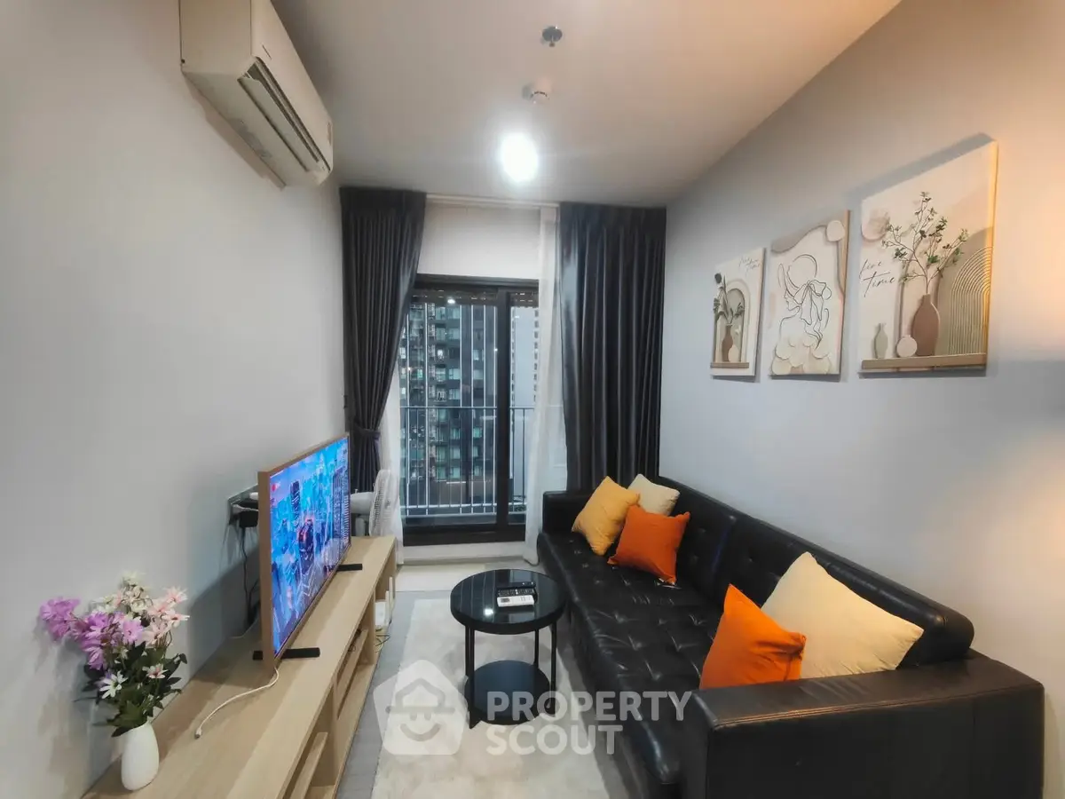 Modern living room with stylish decor and balcony view, featuring a sleek black leather sofa and vibrant cushions.