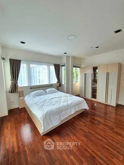 Spacious bedroom with wooden flooring and large windows for natural light.