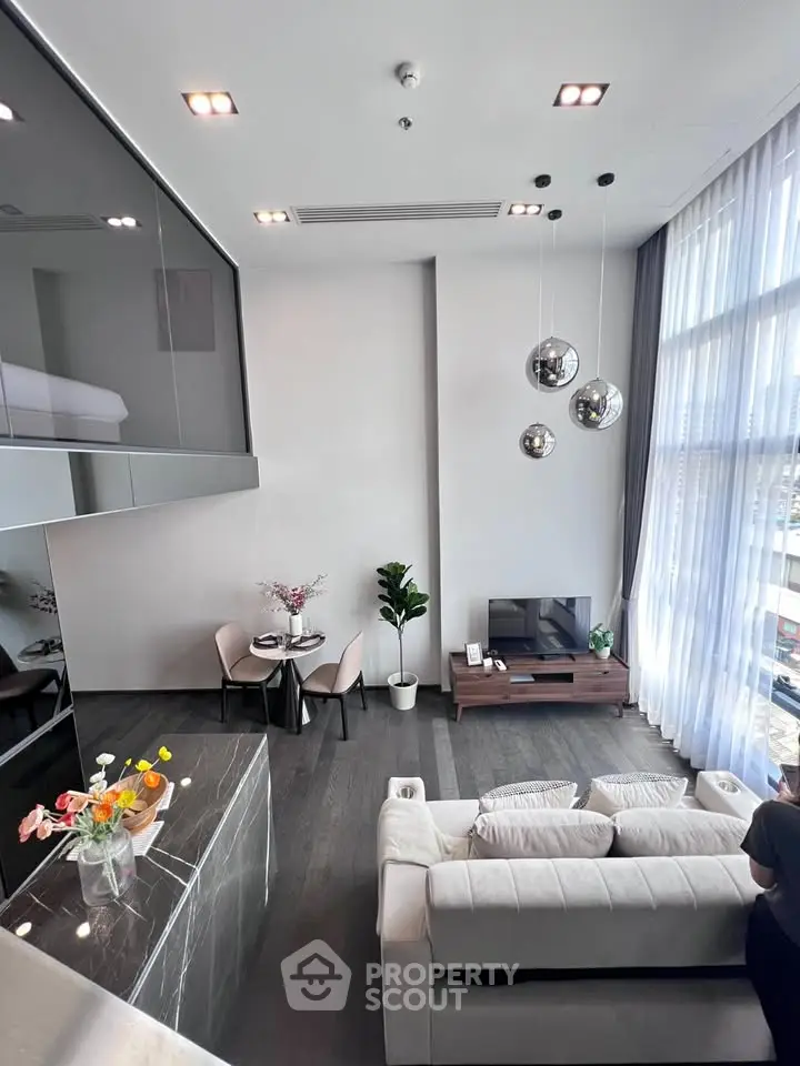 Modern living room with high ceilings, stylish decor, and large windows offering natural light.