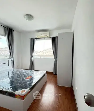 Bright bedroom with wooden flooring, large window, and modern air conditioning unit.