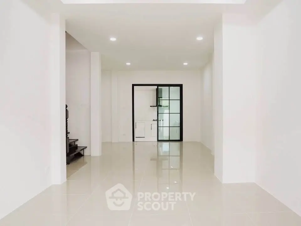 Spacious modern living room with sleek tile flooring and glass door leading to kitchen.