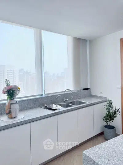 Modern kitchen with sleek countertops and city view, featuring elegant decor and ample natural light.