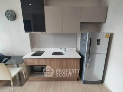 Modern compact kitchen with sleek cabinetry and stainless steel fridge in a stylish apartment.