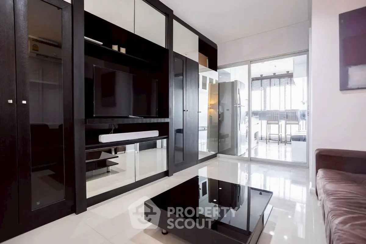 Modern living room with sleek black furniture and large glass doors leading to a bright balcony.