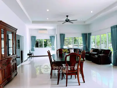 Spacious living room with elegant dining set and large windows offering natural light and garden views.