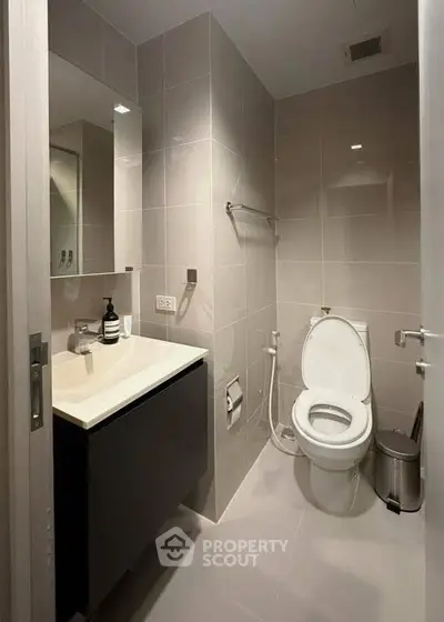 Modern bathroom with sleek fixtures and neutral tiles, featuring a vanity and toilet.