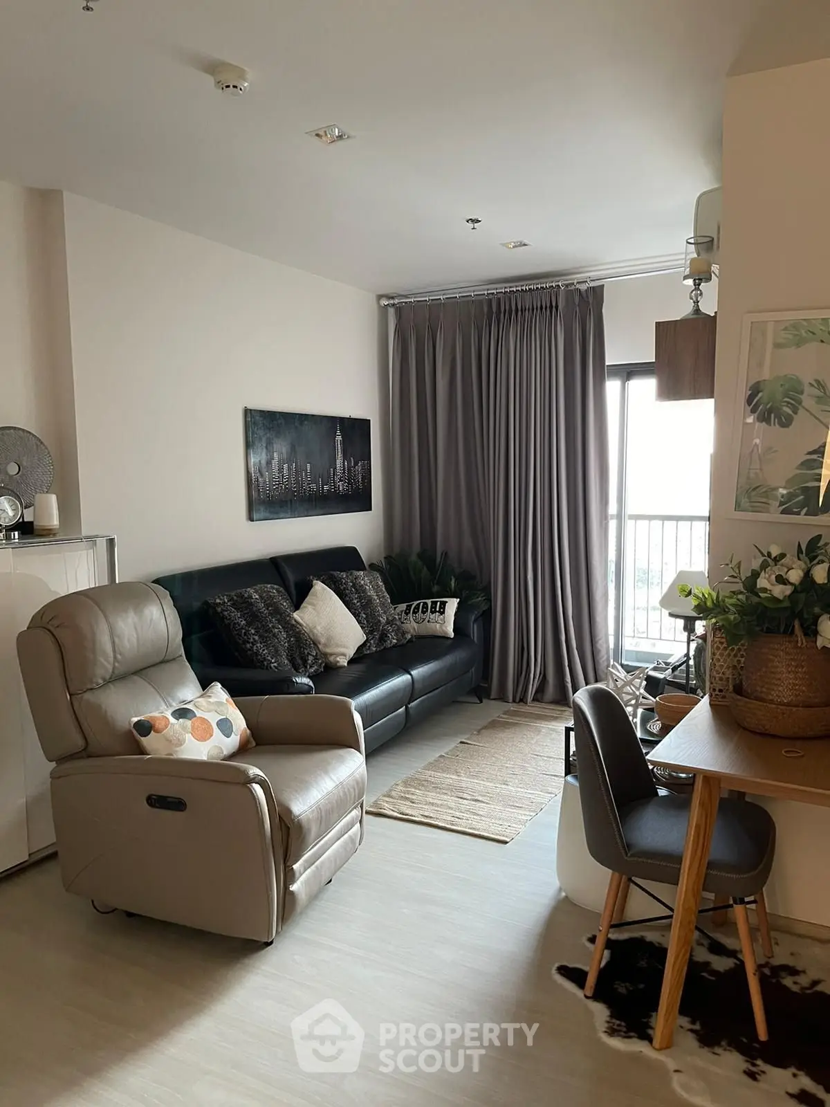 Modern living room with cozy seating and stylish decor, featuring a cityscape artwork and natural light.