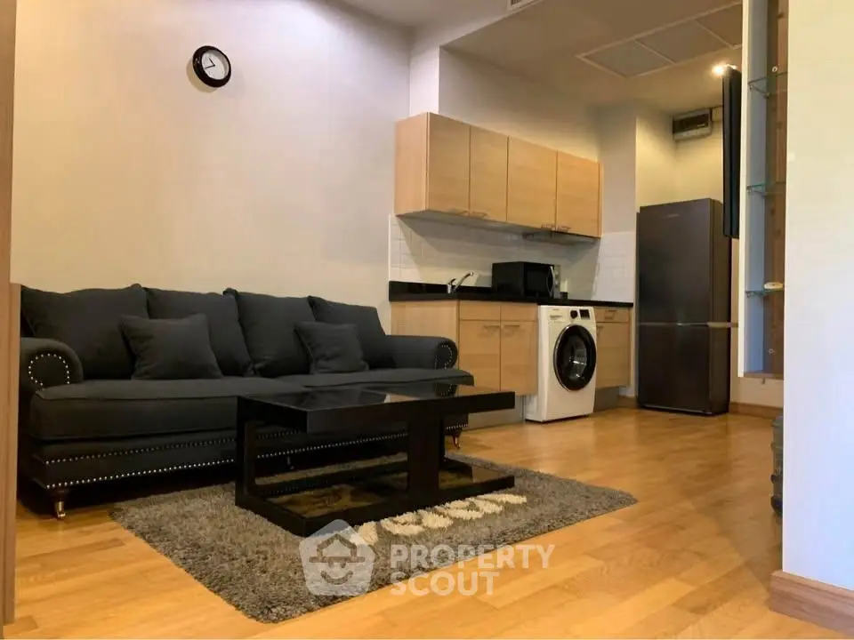 Modern living room with sleek kitchen and washing machine, featuring a stylish black sofa and wooden flooring.
