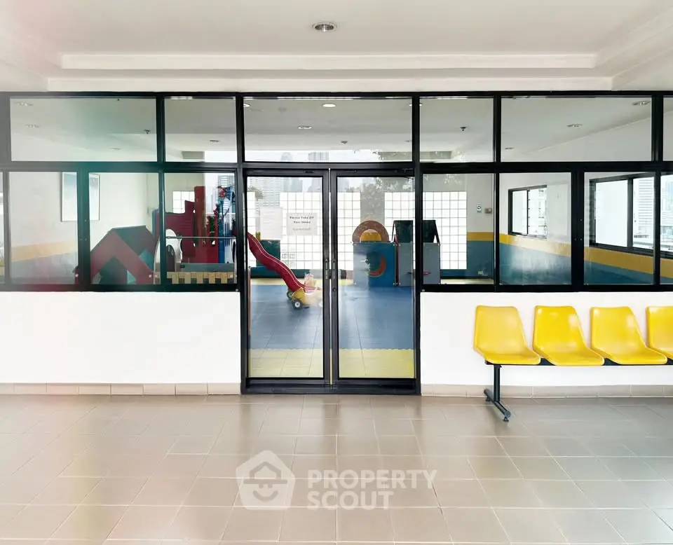 Modern building entrance with glass doors leading to a colorful indoor play area, featuring vibrant seating.
