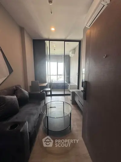 Modern apartment interior with cozy living room and glass partitioned bedroom, featuring stylish furniture and natural light.
