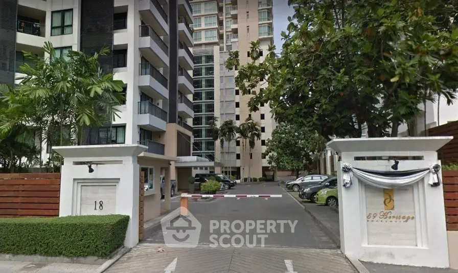Modern condominium entrance with lush greenery and secure parking area.