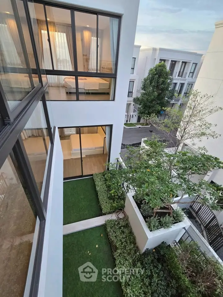 Modern multi-story building with lush green garden and large windows, showcasing contemporary architecture.