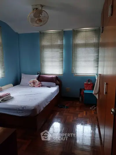 Cozy bedroom with wooden flooring and blue walls, featuring a comfortable bed and ample natural light.