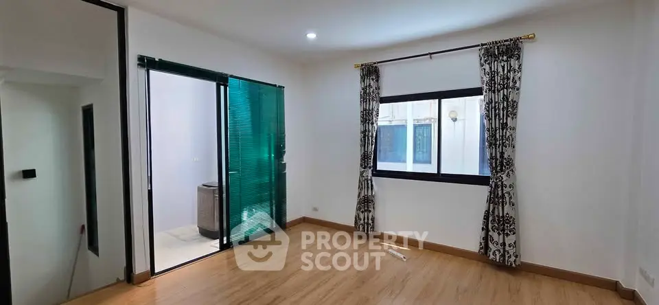 Spacious room with wooden flooring and large window, featuring elegant curtains and glass door leading to balcony.