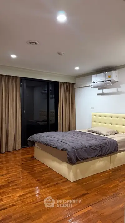 Spacious bedroom with modern design and wooden flooring, featuring a comfortable bed and large windows.