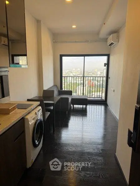 Modern apartment with sleek dark flooring, compact living area, and washing machine, offering a stunning city view.