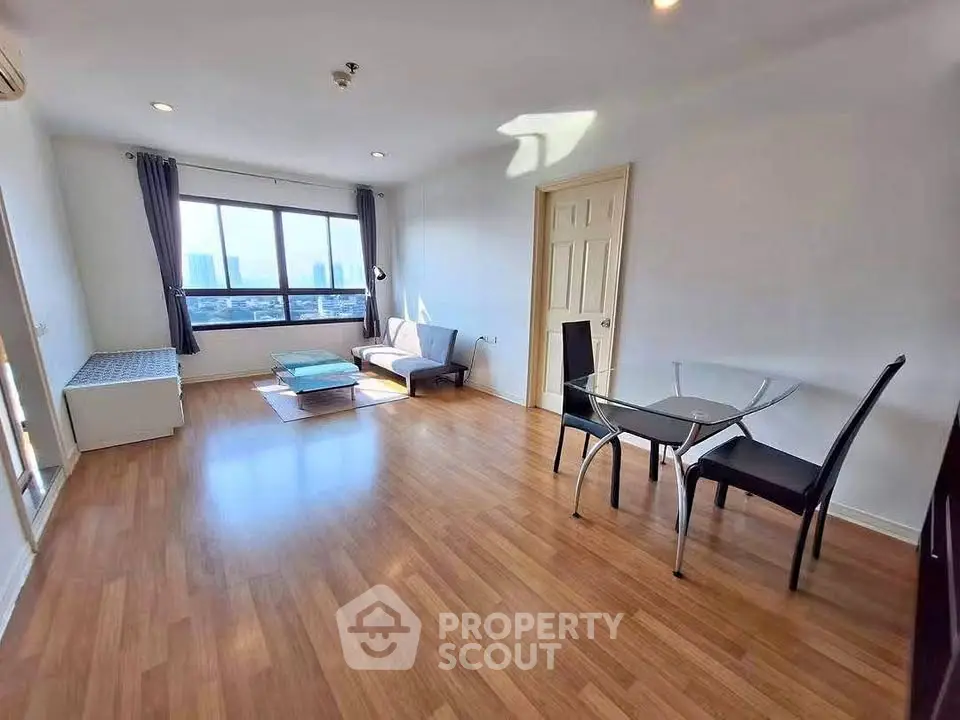 Spacious living room with wooden flooring and city view, featuring modern furniture and ample natural light.
