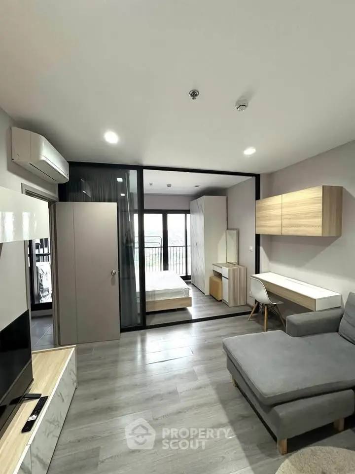 Modern apartment interior with open living room and bedroom, featuring sleek furniture and large windows.