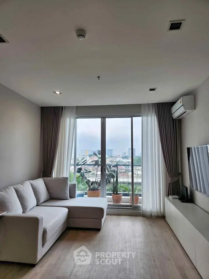 Modern living room with large window and city view, featuring a cozy sofa and sleek TV setup.