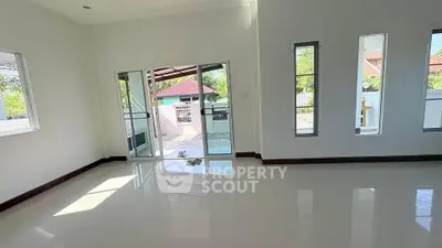 Spacious living room with glossy floors and large windows opening to a patio with garden view.