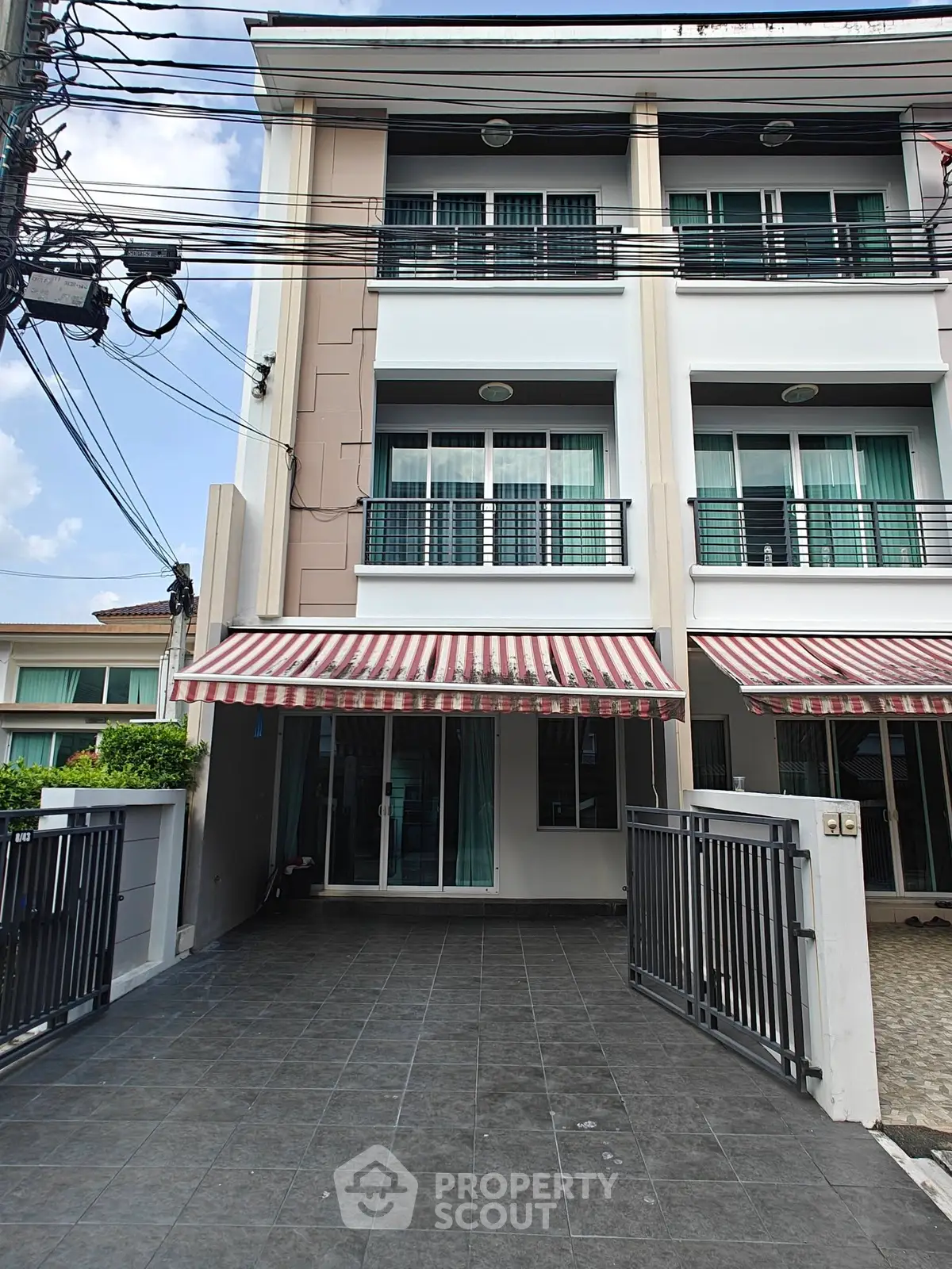 Modern three-story townhouse with gated driveway and striped awnings, perfect for urban living.