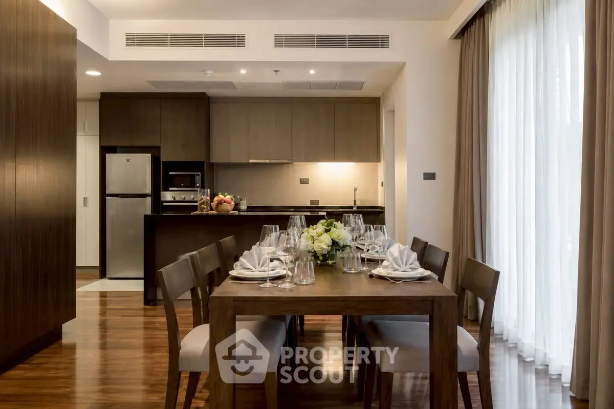 Elegant dining area with modern kitchen, featuring wooden furniture and floor-to-ceiling windows.