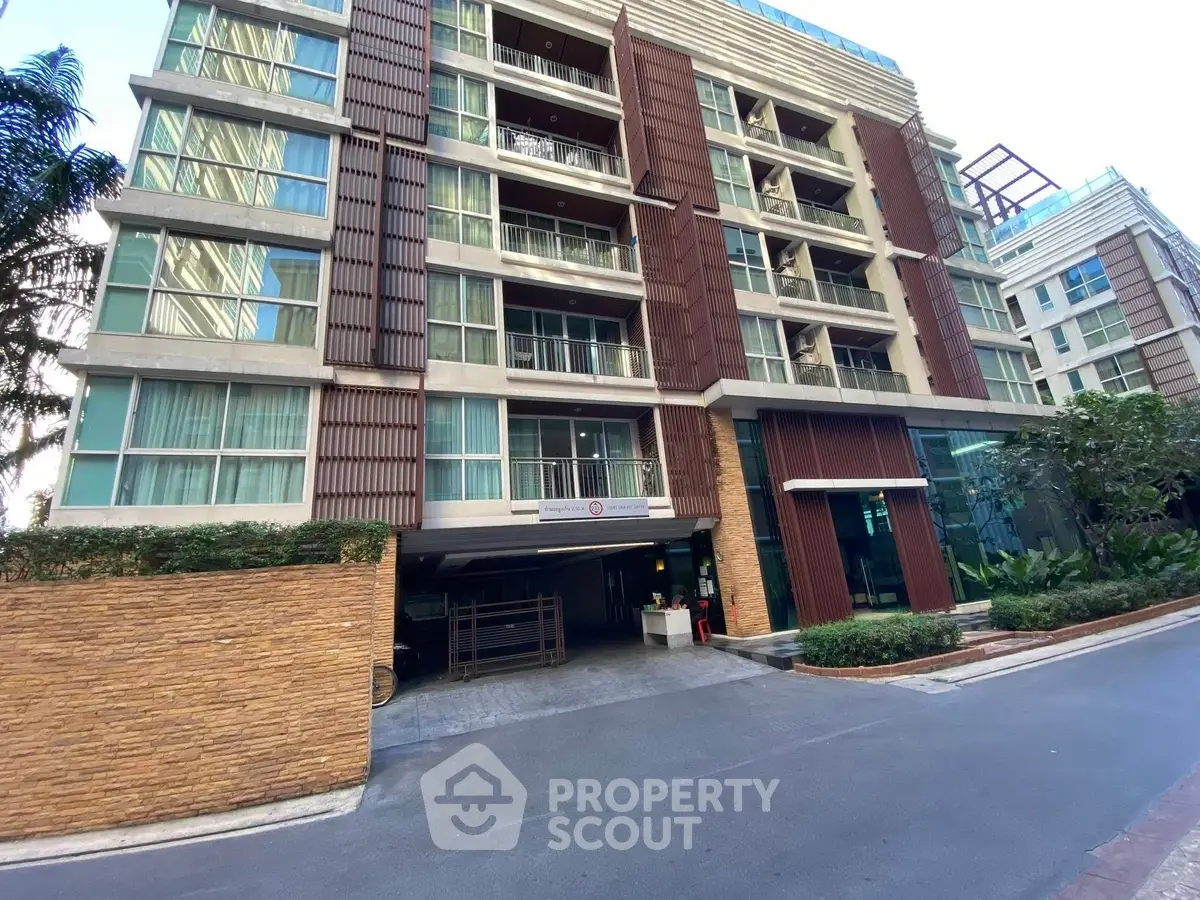 Modern multi-story residential building with glass balconies and lush landscaping.