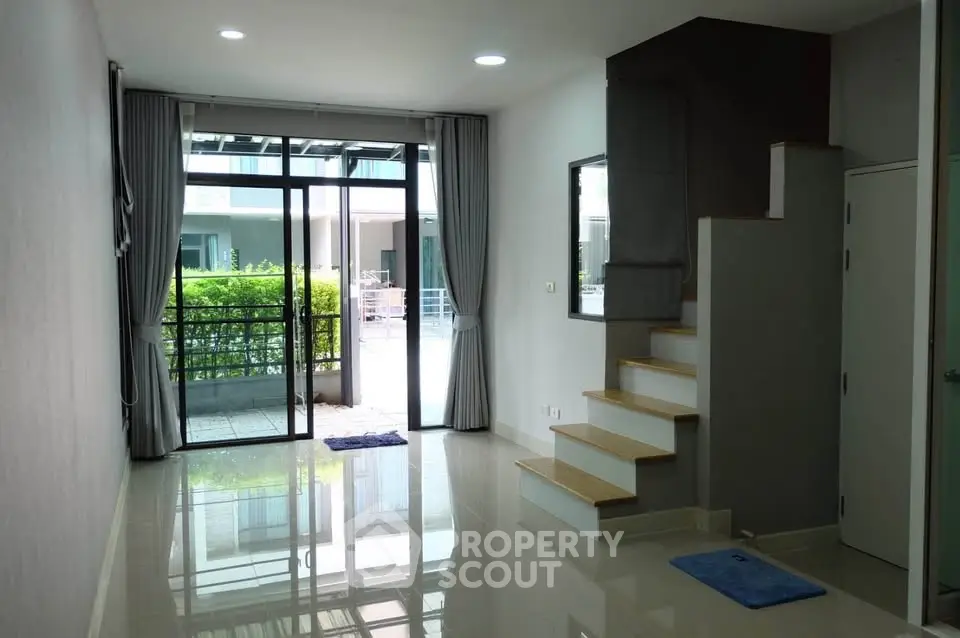 Spacious modern living room with large windows and garden view, featuring sleek staircase and glossy tiled floor.