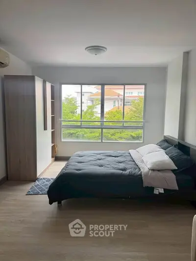 Spacious bedroom with large window and modern furnishings, offering a serene view.