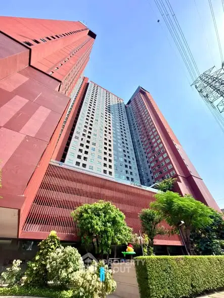 Stunning modern high-rise building with lush greenery and vibrant red facade, perfect for urban living.
