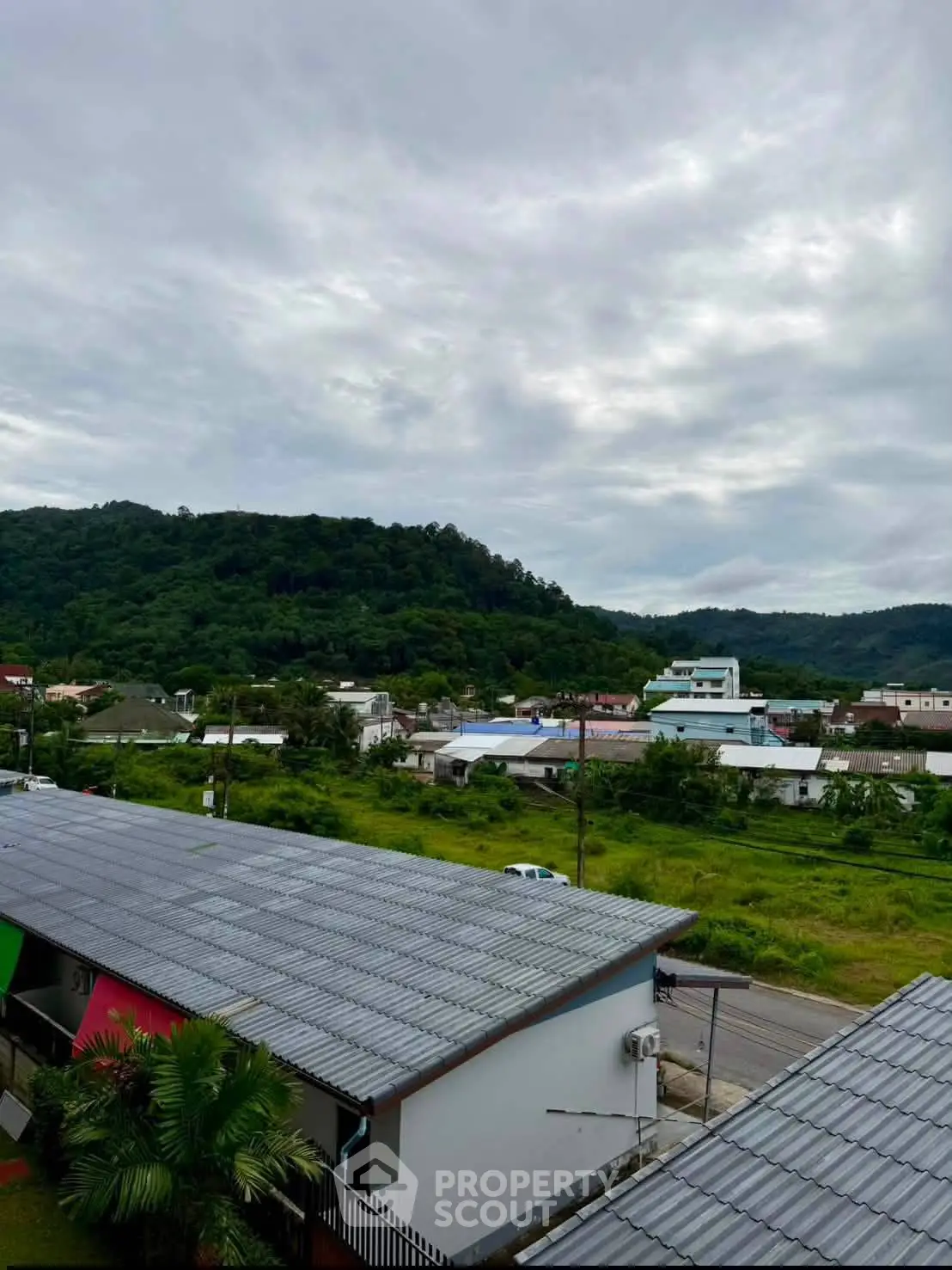 Scenic view of residential area with lush green hills and cloudy sky backdrop.