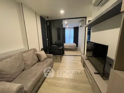 Modern living room with cozy sofa and TV, open view to bedroom, sleek design.