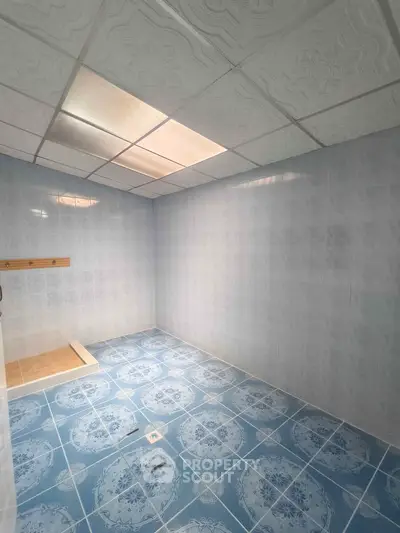 Spacious tiled bathroom with blue patterned floor and white ceiling tiles.